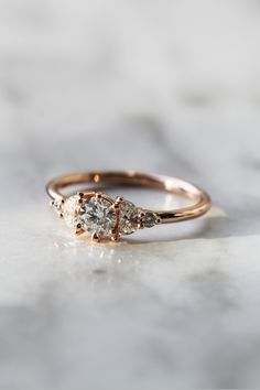 a three stone ring with two diamonds on it, sitting on a marble countertop