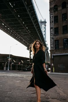 a woman standing in the middle of an empty parking lot with a bridge behind her