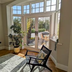 a chair sitting in front of a window next to a potted plant on top of a rug