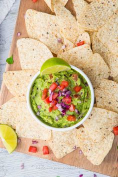 guacamole in a white bowl surrounded by tortilla chips on a cutting board