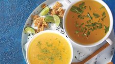 two bowls of soup on a plate with spoons