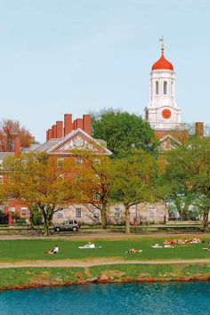 people laying on the grass in front of a large building with a clock tower above it