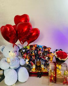 a teddy bear sitting next to some heart shaped balloons and other items on a table