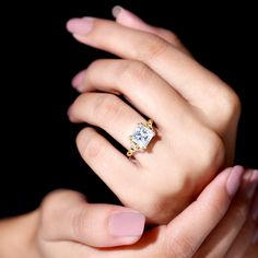 a woman's hand with pink manicured nails holding a ring that has a diamond on it