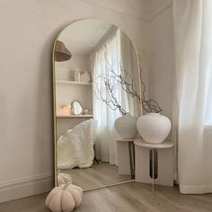 a mirror sitting on top of a wooden floor next to a white vase filled with flowers