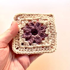 a hand holding a crocheted square with a flower on it's center