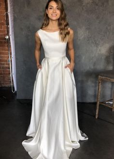 a woman standing in front of a brick wall wearing a white dress and smiling at the camera