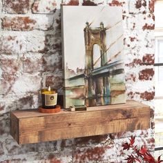 a painting on a brick wall next to a wooden shelf with a cup and candle