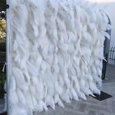 white feathers are stacked on top of each other in front of a metal pole and fence