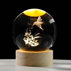 a glass ball with flowers in it sitting on a wooden stand next to a black background