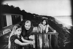 an old black and white photo of three people sitting at a table near the ocean