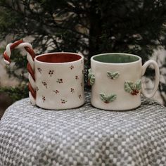 two coffee mugs sitting on top of a table next to each other with candy canes sticking out of them