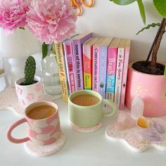 pink flowers are in vases next to two mugs and books on a table