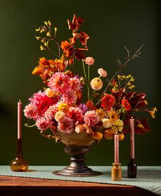 a vase filled with lots of colorful flowers on top of a table next to candles