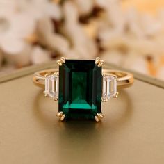 an emerald and diamond ring sitting on top of a table