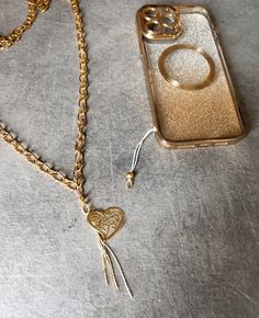 a gold phone case with a heart shaped keychain and chain attached to it