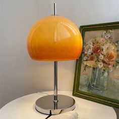 a yellow lamp sitting on top of a white table next to a framed flower arrangement