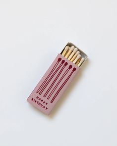 a pink birthday matchbox filled with matchesticks on top of a white surface