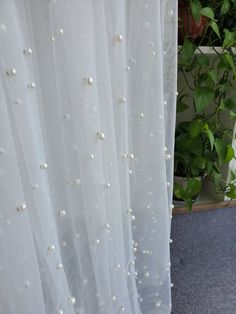 white sheer curtains with pearls on them in front of a potted plant and window