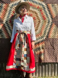 a woman wearing a hat and dress standing in front of a quilt