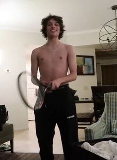 a shirtless young man holding a tennis racquet in his hand while standing in a living room