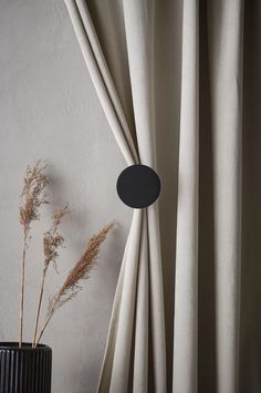 a black vase sitting next to a window covered in white drapes and a plant