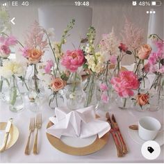 the table is set with pink and white flowers in glass vases, silverware, and napkins