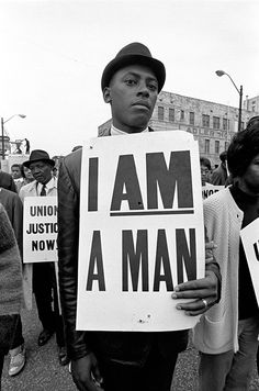 a man holding a sign that says i am a man in front of other people