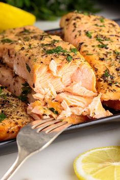 two pieces of salmon on a plate with lemons and parsley