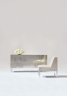 a white chair sitting next to a silver cabinet with flowers on it's top