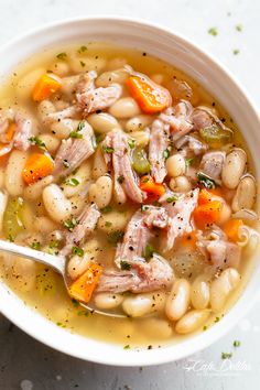 a white bowl filled with meat and bean soup on top of a table next to a spoon