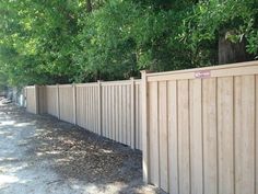 a wooden fence is lined with trees and gravel