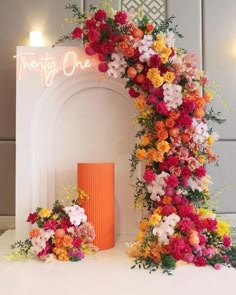 a white table topped with an orange vase filled with flowers and a neon sign that says twenty one