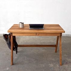 a wooden table with a laptop and coffee cup on it, next to a wall