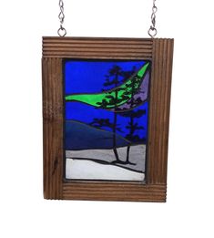 a stained glass window hanging from a chain on a white wall, with trees in the background