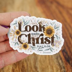 a hand holding a sticker with the words look into christ written in sunflowers