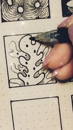 a person using a pen to draw designs on a piece of paper with black ink