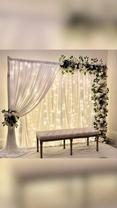 a wedding ceremony setup with white flowers and greenery on the wall, along with a bench