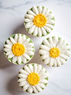 three cupcakes decorated with white and yellow flowers on top of a marble table