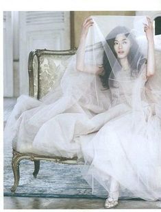 a woman in a white dress sitting on a chair with a veil over her head