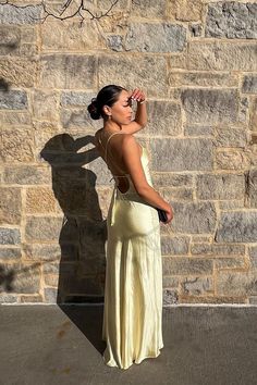 a woman standing in front of a stone wall talking on a cell phone while wearing a yellow dress