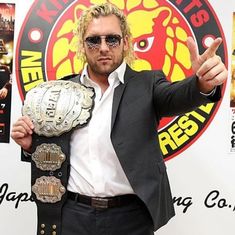 a man in a suit and sunglasses holds up his wrestling belt while posing for the camera