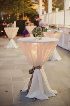 the table is set up with white linens and flowers on it for an outdoor function