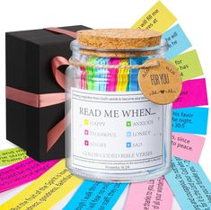 a jar filled with lots of different colored papers next to a black box and colorful ribbons