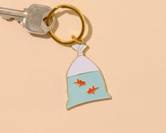 a keychain with a bag and two goldfish in it on a beige background