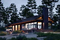 a modern cabin style home in the woods at night with its lights on and windows open