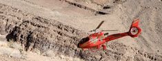 a red helicopter is flying over the desert