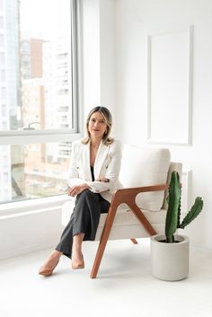 a woman sitting on a white couch next to a cactus in a pot and window