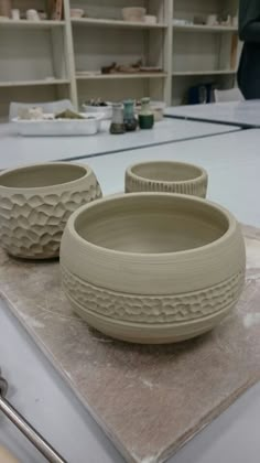 three clay bowls sitting on top of a table in a room with shelves behind them