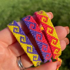 two colorful bracelets in the palm of someone's hand with grass in the background